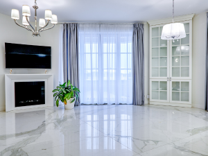 Bright modern living room with a wall-mounted TV above a white fireplace, and a potted plant on the marble floor.